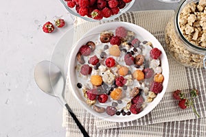 Granola crispy honey muesli with natural yogurt, fresh red and yellow raspberries, chocolate and nuts in a bowl on gray background