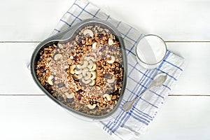 Granola in a heart-shaped baking sheet, a glass of yogurt. White background. Food Concept