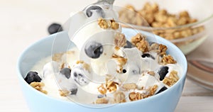 Granola is mixed with a spoon with yogurt and blueberries.