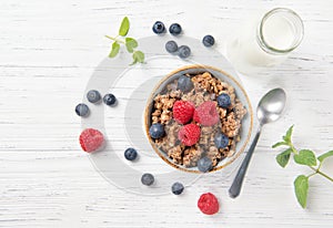 Granola muesli, milk and ripe blueberries and raspberries, healthy breakfast concept, wooden background, top view