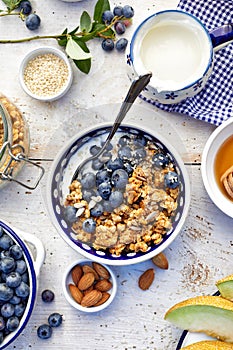 Granola with natural yogurt, fresh blueberries, nuts and honey in a ceramic bowl on a white wooden table. Delicious breakfast or d