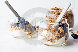 Granola with nuts, yogurt and berries in jar. Breakfast parfait with muesli, yoghurt and blueberries, white background