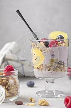 Granola with raspberries, blueberries and golden kiwi. Glass of muesli, berries and yogurt parfait on the table. Breakfast sweet
