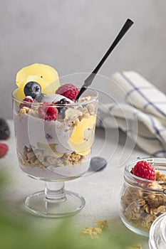 Granola with raspberries, blueberries and golden kiwi. Glass of muesli, berries and yogurt parfait on the table. Vegan natural