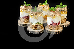 Granola, slices of different fresh fruits and berries, yogurt, honey in jars isolated on black background.