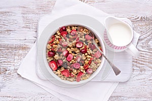 Granola in a white bowl with jug of milk on a rustic wooden table, top view with copy space