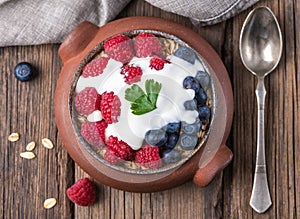 Granola with white yogurt with raspberries and blueberries in ceramic bowl on natural wooden background