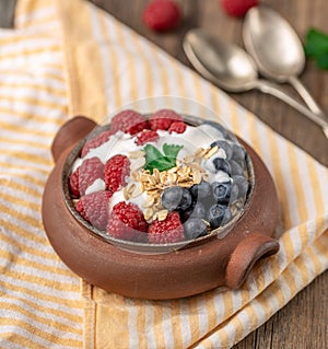 Granola with white yogurt with raspberries and blueberries in ceramic bowl on stripped napkin
