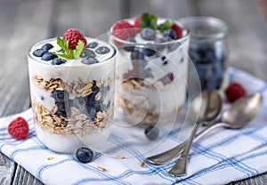 Granola with white yogurt with raspberries and blueberries in two glasses on blue napkin