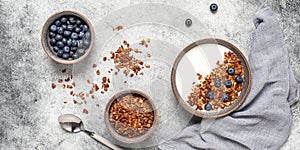 Granola with yogurt and blueberries in a bowl on a gray grunge background. Healthy tasty breakfast. Top view, flat lay, banner