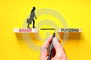 Grant funding symbol. Concept words Grant funding on wooden blocks. Beautiful yellow table yellow background. Businessman hand.
