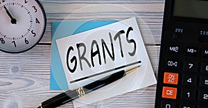 GRANTS - word on a white sheet on the background of a calculator, alarm clock and pen