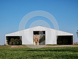 Granular old photo of round hay bales stacked in a sheet metal tin barn on a rural farm.