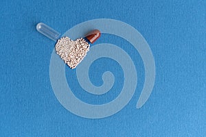 Granules poured from a heart-shaped capsule on a classic blue background. Heart shaped medicines. Heart symbol drawn by
