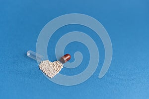 Granules poured from a heart-shaped capsule on a classic blue background. Heart shaped medicines. Heart symbol drawn by