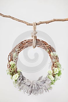 A grape cradle ring hanging on a rope on a stick, decorated with green flowers and leaves with a gray wool rug