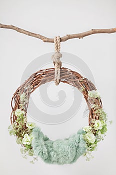 A grape cradle ring hanging on a rope on a stick, decorated with green flowers and leaves with a green wool rug