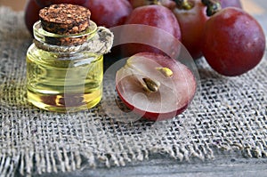 Grape seed oil in a glass jar and fresh grapes on burlap cloth background.Bottle of organic grape seed oil for spa and bodycare.