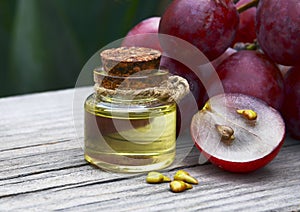 Grape seed oil in a glass jar and fresh grapes on old wooden table. Bottle of organic grape seed oil for spa and bodycare.