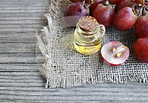 Grape seed oil in a glass jar and fresh grapes on old wooden table.Bottle of organic grape seed oil for spa and bodycare.