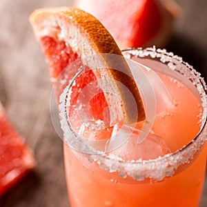 Grapefruit cocktail with ice and salt on a wooden background. Party time. square