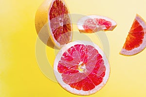 Grapefruit cut into different parts and soars in the air on yellow isolated background.
