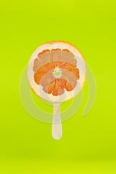 Grapefruit icecream with wood stick on light green background. Creative summe fruity popsicle sticks