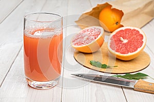Grapefruit juice in a glass on a wooden table, fresh cut oranges in the background