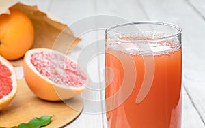 Grapefruit juice in a glass on a wooden table, fresh cut oranges in the background