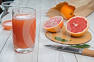 Grapefruit juice in a glass on a wooden table, fresh oranges in the background