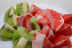 Grapefruit and kiwi cut into wedges on a white plate. Still life.