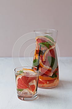 Grapefruit lemonade with green mint in glasses and jug on beige background.