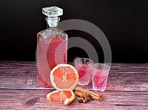 Grapefruit liqueur with cinnamon and anise, strong homemade alcohol in a crystal decanter and two glasses on a dark wooden table