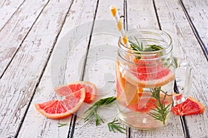 Grapefruit and rosemary infused detox water in a mason jar against white wood