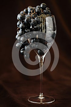 Grapes in red wine glass hanging over against brown background