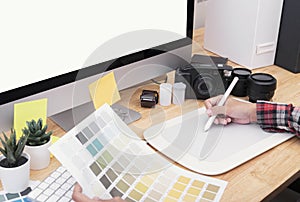 Graphic designer artist using graphics tablet drawing and looking at colour chart his work at desk in office