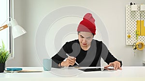 A Graphic designer man in red wool hat retoucher working with tablet and stylus pen.