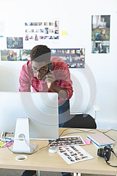 Graphic designer talking on mobile phone while working on computer at desk