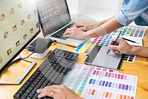 Graphic designer team working on web design using color swatches editing artwork using tablet and a stylus At Desks In Busy