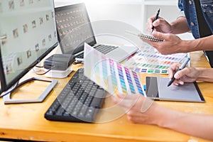 graphic designer team working on web design using color swatches editing artwork using tablet and a stylus At Desks In Busy