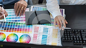 Graphic designer team working on web design using color swatches editing artwork using tablet and a stylus at desks In creative