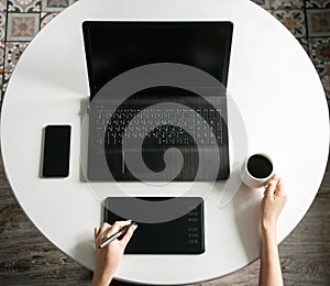 Graphic designer working at a white table using laptop and graphics tablet. Famale hands.