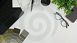 Graphic designer workspace with notebook, glasses, houseplant, smart phone keyboard and color swatches.