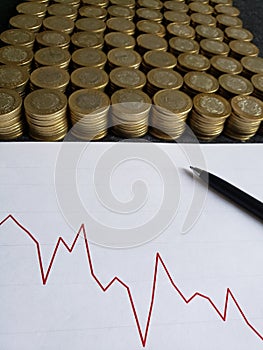 graphic with a downward trend line, black pen and stacked coins of mexican pesos