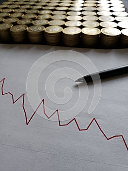 graphic with a downward trend line, black pen and stacked coins of mexican pesos