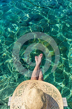 Graphic image of top down view of woman wearing big summer sun hat relaxing on small wooden pier by clear turquoise sea