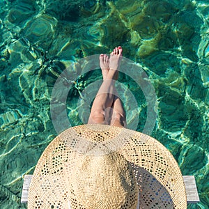 Graphic image of top down view of woman wearing big summer sun hat relaxing on small wooden pier by clear turquoise sea