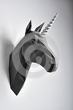 Graphitic black coloured paper unicorn`s head hanging on white wall.