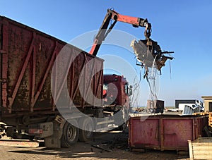 A grapple truck loads scrap industrial metal for recycling.