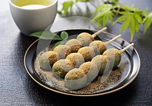 Grass dumplings covered with soybean flour and green tea served on a black plate set against a black background